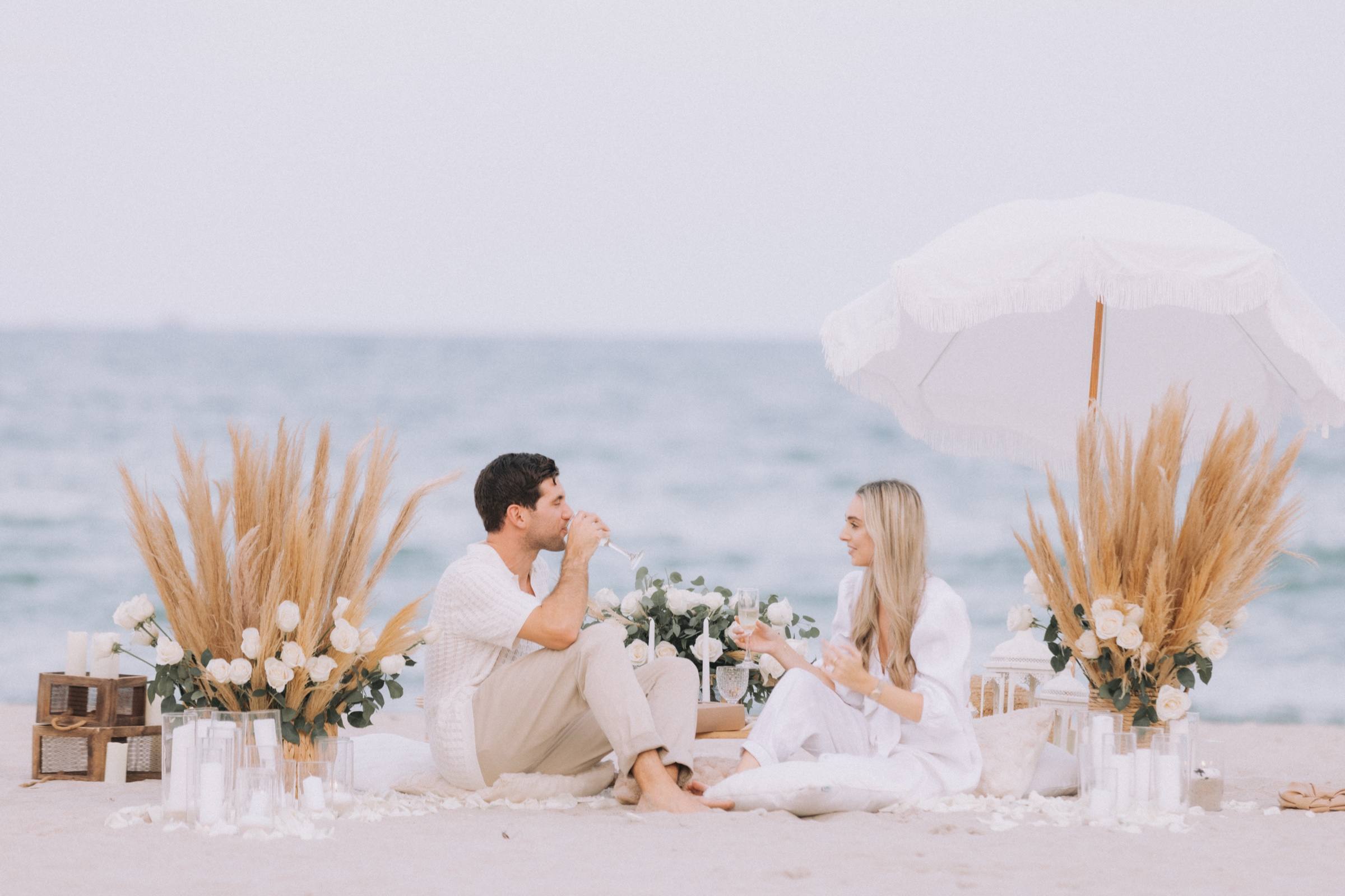 Couple at a white beach picnic with pampas grass, white roses and a parasol
