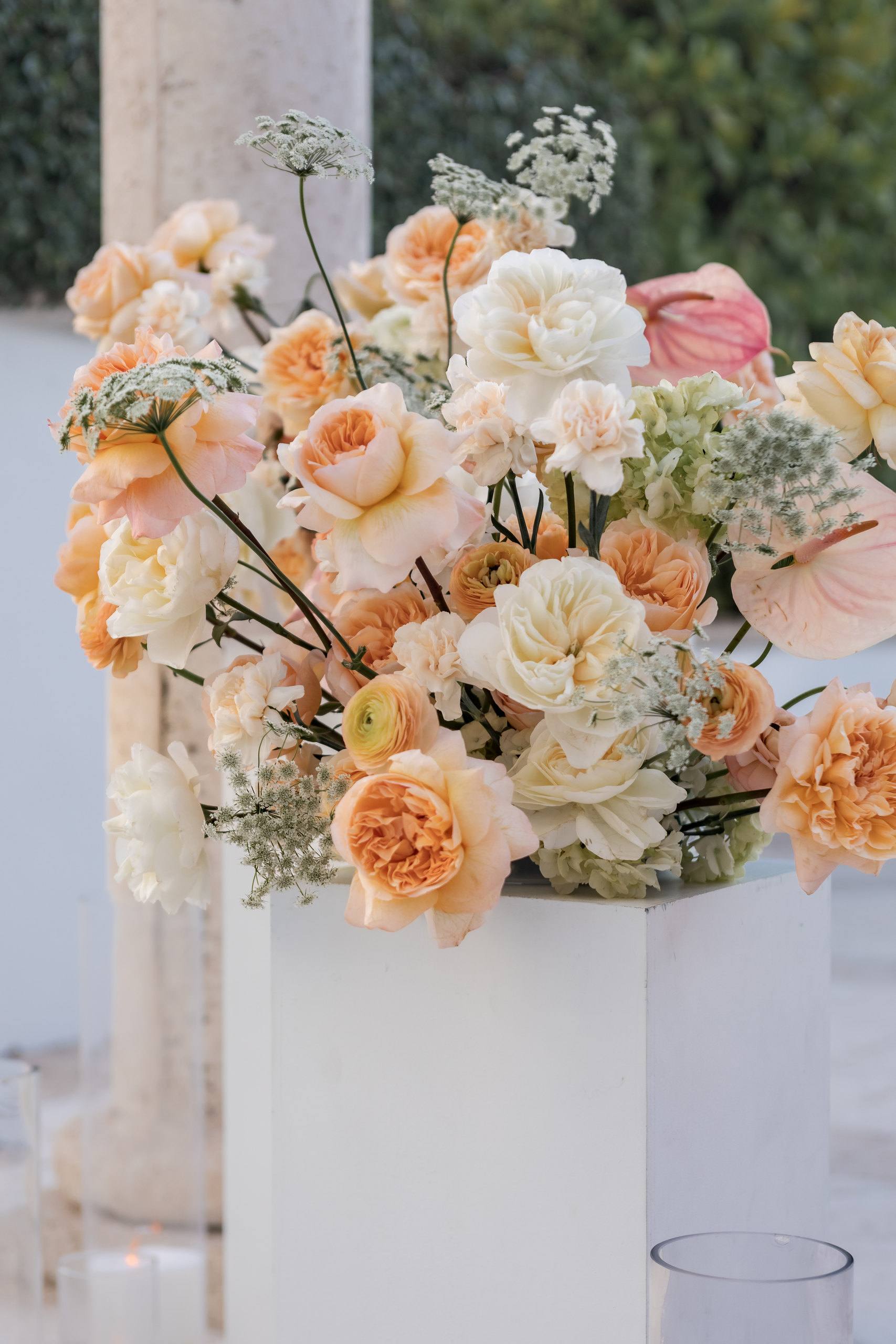 Peach and cream flowers on a white column beside the aisle