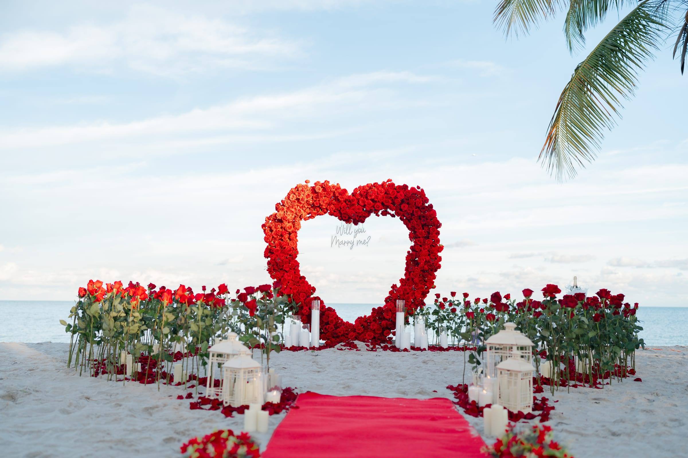 Heart shaped arch of red roses at the end of a rose lined aisle on the beach