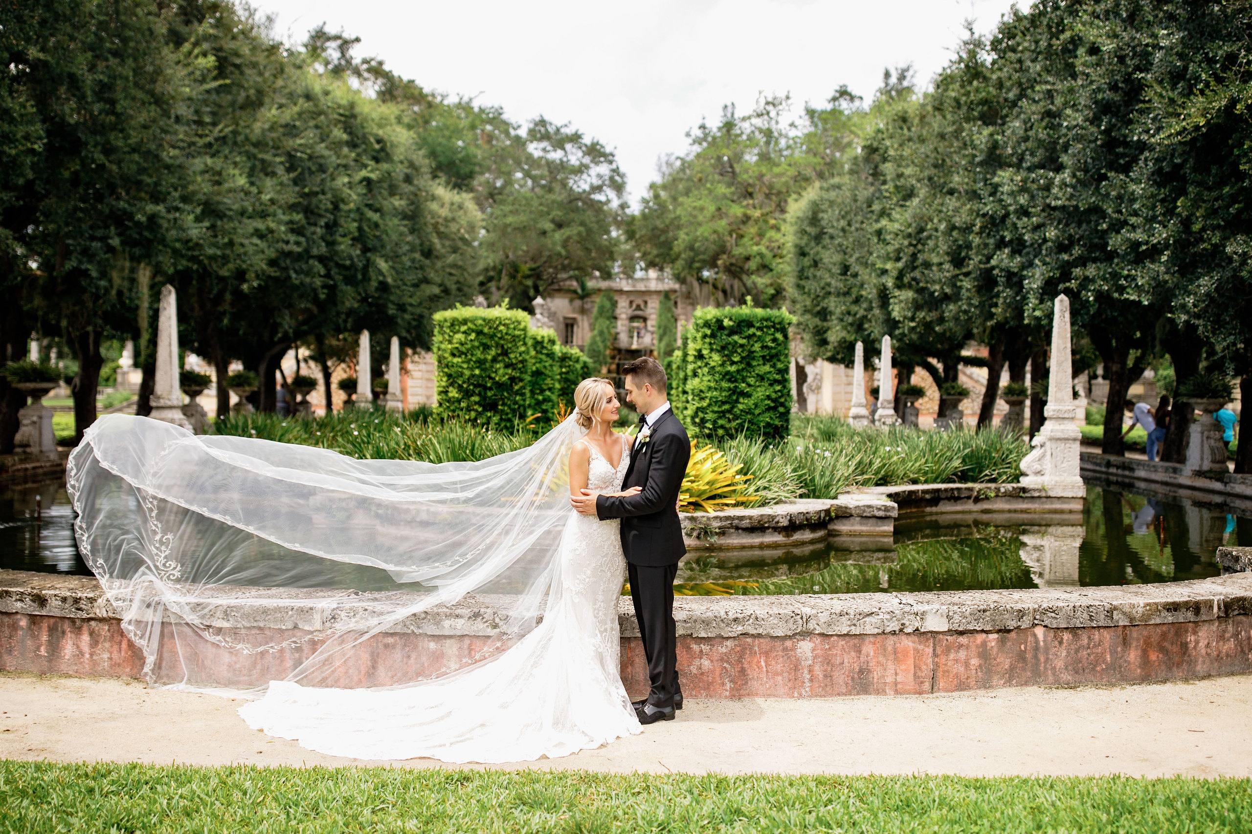 Couple beneath a flowing veil beside a garden lake