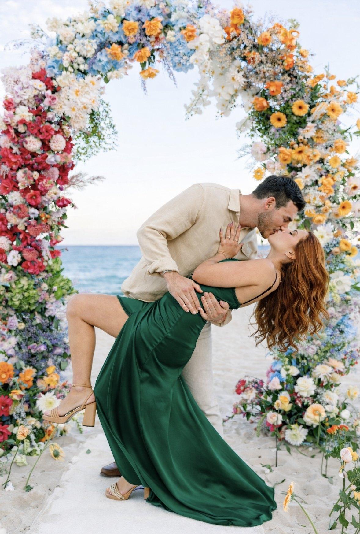 Couple kissing under a colorful floral arch on the beach